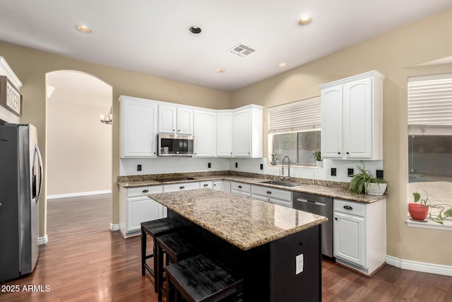 kitchen featuring stainless steel appliances, a sink, arched walkways, a kitchen bar, and light stone counters