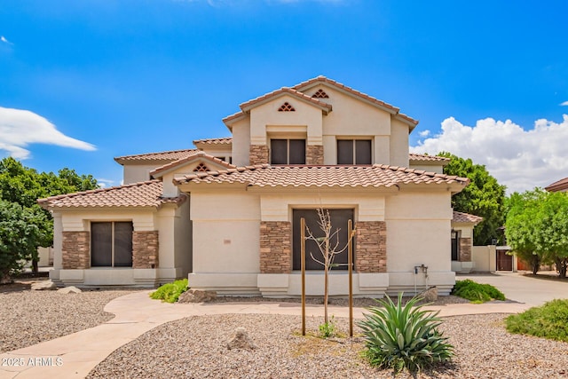mediterranean / spanish-style home with stone siding, stucco siding, a tiled roof, and fence