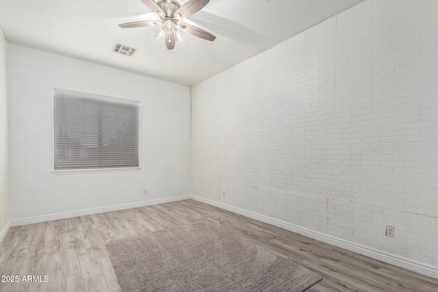 spare room with wood finished floors, baseboards, ceiling fan, and brick wall