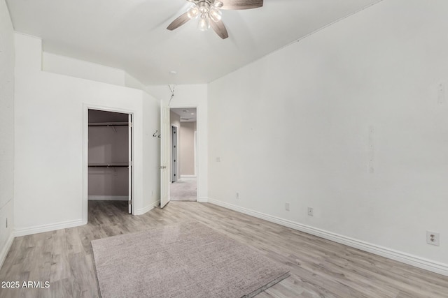unfurnished bedroom with light wood-type flooring, baseboards, a walk in closet, a closet, and ceiling fan