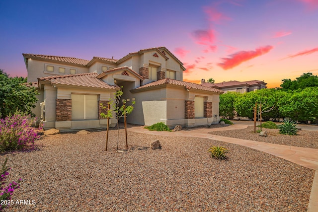 mediterranean / spanish home featuring a tile roof, stucco siding, and stone siding
