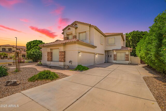 mediterranean / spanish home with a tile roof, stucco siding, concrete driveway, an attached garage, and fence