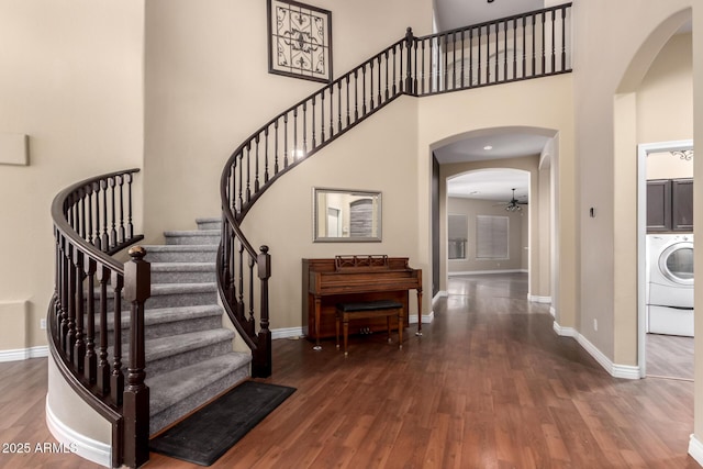 entryway with washer / clothes dryer, arched walkways, wood finished floors, stairway, and a towering ceiling