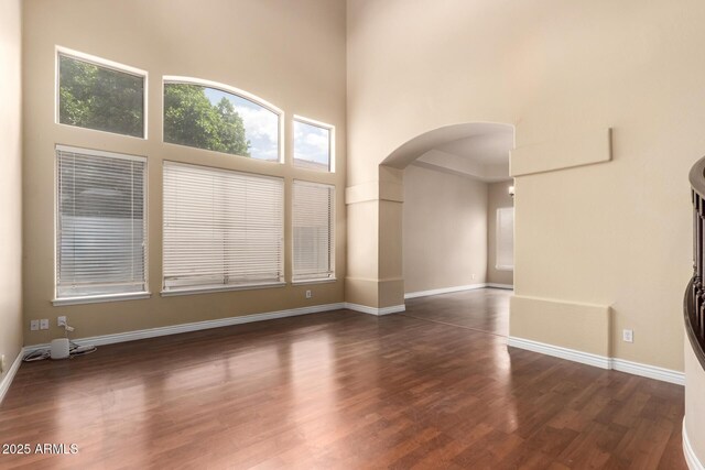 unfurnished living room with arched walkways, dark wood-style floors, a high ceiling, and baseboards