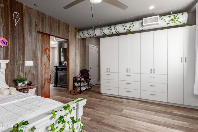 bedroom featuring ceiling fan, light wood-type flooring, and wood walls