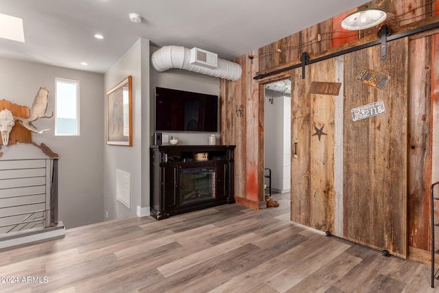 unfurnished living room with wooden walls, hardwood / wood-style flooring, and a barn door