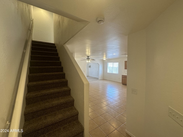 stairs with tile patterned flooring, a textured ceiling, and ceiling fan