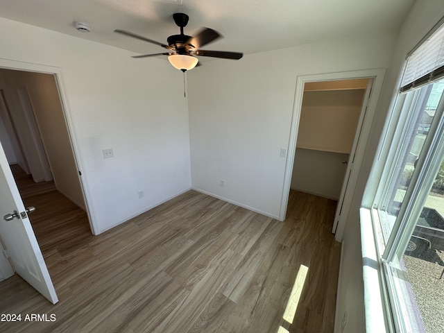 unfurnished bedroom featuring a spacious closet, a closet, ceiling fan, and light wood-type flooring