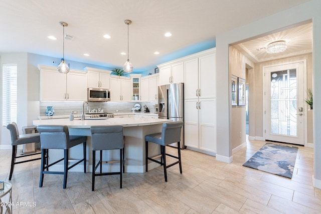 kitchen featuring appliances with stainless steel finishes, a kitchen island with sink, pendant lighting, and white cabinetry