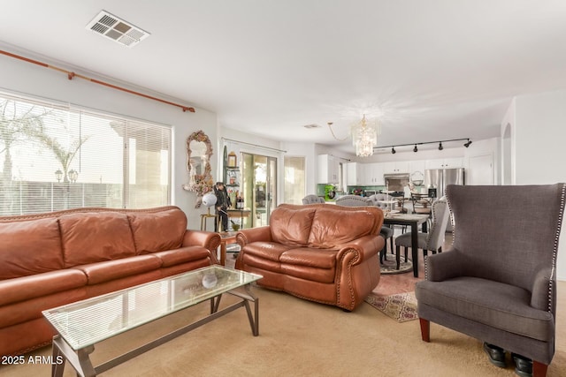 living room featuring light colored carpet, visible vents, rail lighting, and an inviting chandelier