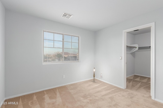 unfurnished bedroom featuring light carpet, a spacious closet, visible vents, and baseboards