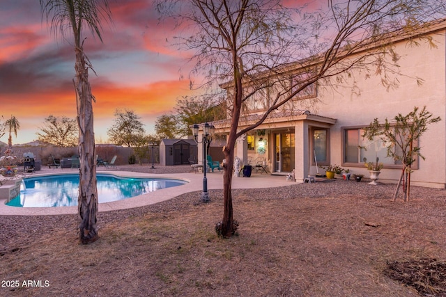 pool at dusk with an outbuilding, a patio, a fenced backyard, a fenced in pool, and a storage unit