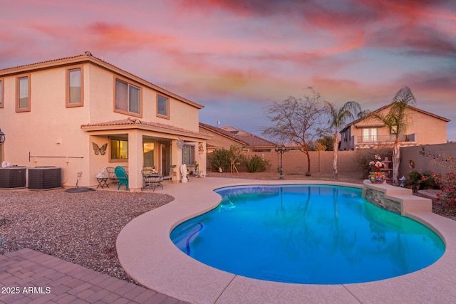 pool at dusk with a patio, central AC, a fenced backyard, and a fenced in pool