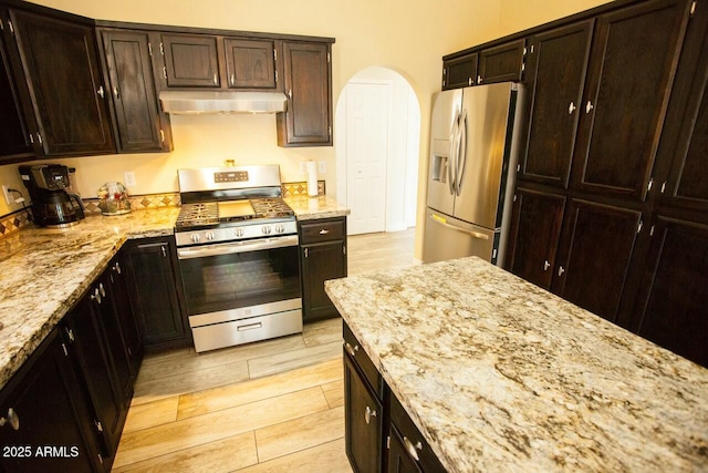 kitchen with stainless steel appliances, dark brown cabinets, and light stone counters