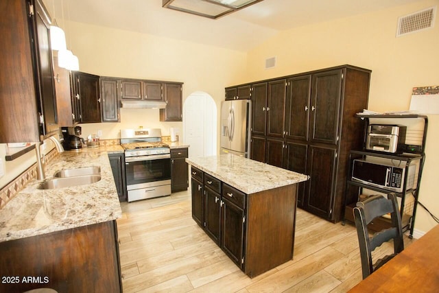 kitchen with a kitchen island, appliances with stainless steel finishes, sink, light stone countertops, and dark brown cabinets