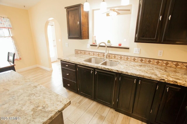 kitchen with sink, hanging light fixtures, dark brown cabinetry, light hardwood / wood-style floors, and light stone countertops