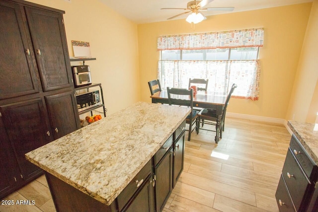 kitchen with light stone counters, a center island, dark brown cabinets, ceiling fan, and light hardwood / wood-style floors