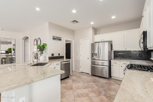 kitchen with appliances with stainless steel finishes, light stone countertops, white cabinets, sink, and kitchen peninsula