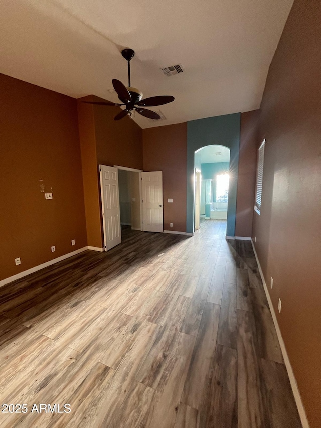interior space featuring ceiling fan, visible vents, arched walkways, wood finished floors, and baseboards