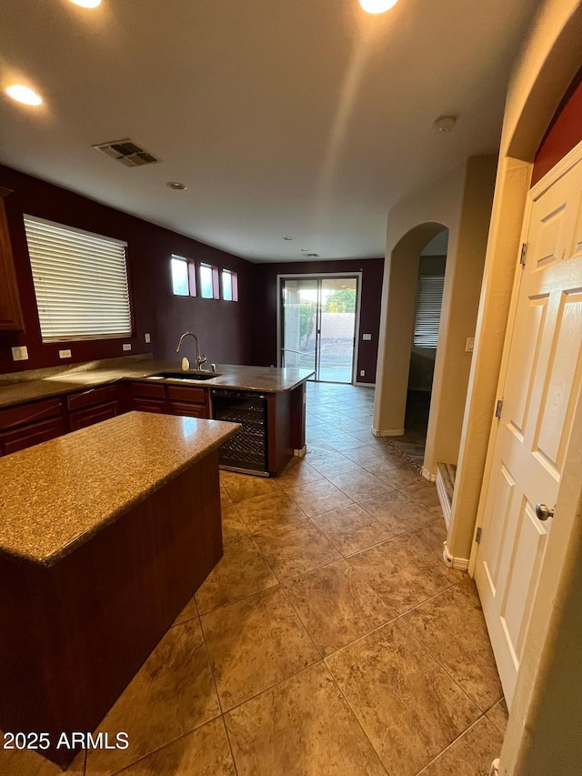 kitchen with visible vents, arched walkways, light stone countertops, a sink, and a peninsula