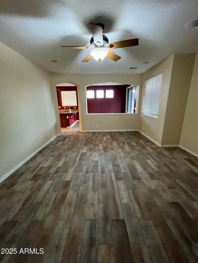 unfurnished room with baseboards, a ceiling fan, arched walkways, and wood finished floors