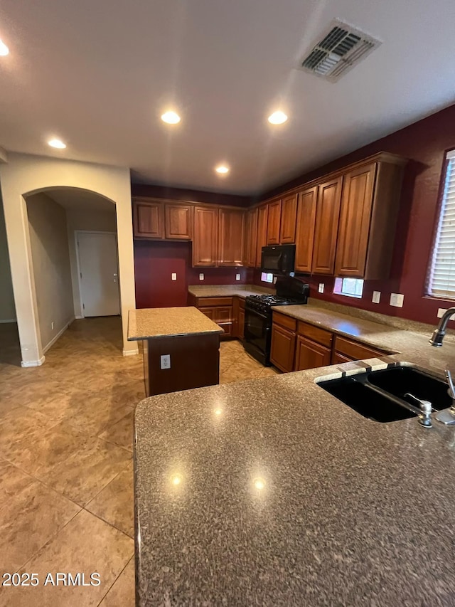kitchen with brown cabinetry, visible vents, arched walkways, a sink, and black appliances