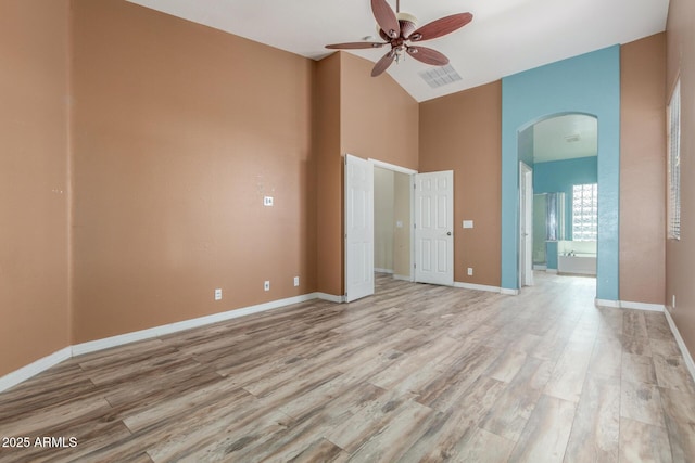 interior space featuring light wood finished floors, arched walkways, high vaulted ceiling, ensuite bathroom, and visible vents