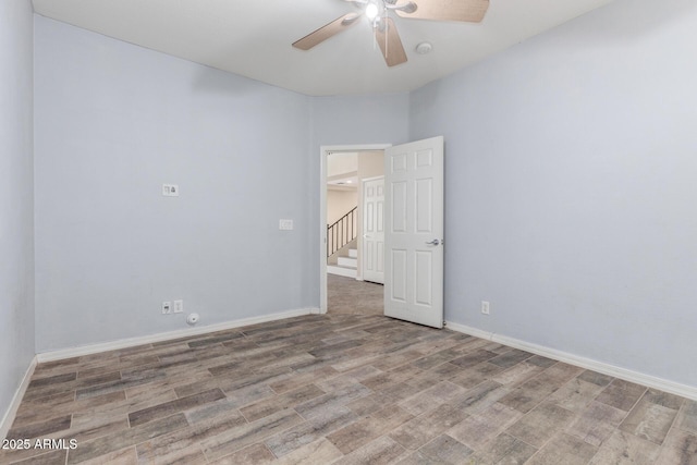 unfurnished room featuring baseboards, a ceiling fan, wood finished floors, and stairway