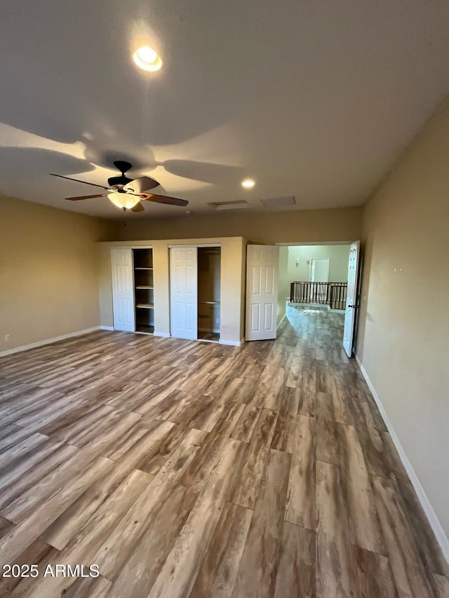 unfurnished bedroom featuring multiple closets, baseboards, recessed lighting, and wood finished floors