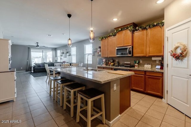 kitchen featuring light tile patterned floors, stainless steel microwave, a kitchen bar, and a sink