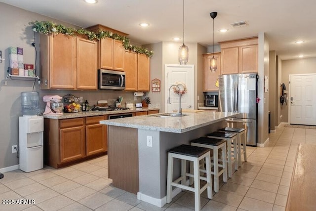 kitchen featuring visible vents, light stone counters, a breakfast bar, stainless steel appliances, and a sink