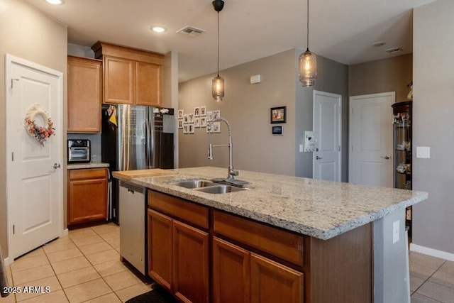 kitchen featuring light tile patterned floors, an island with sink, appliances with stainless steel finishes, hanging light fixtures, and a sink