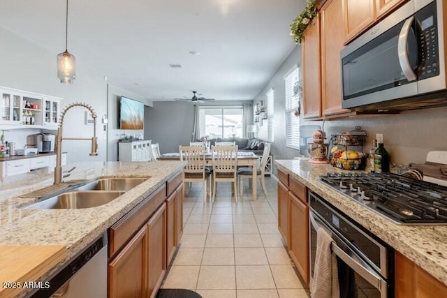 kitchen with light tile patterned floors, light stone counters, a sink, open floor plan, and appliances with stainless steel finishes