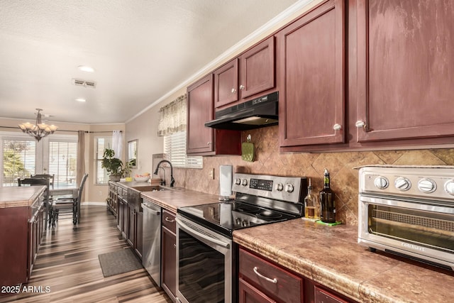 kitchen featuring hardwood / wood-style floors, appliances with stainless steel finishes, sink, ornamental molding, and a notable chandelier