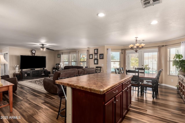 kitchen featuring dark hardwood / wood-style floors, a kitchen island, a kitchen bar, a textured ceiling, and ceiling fan with notable chandelier