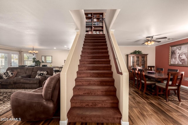 staircase featuring crown molding, ceiling fan with notable chandelier, and wood-type flooring