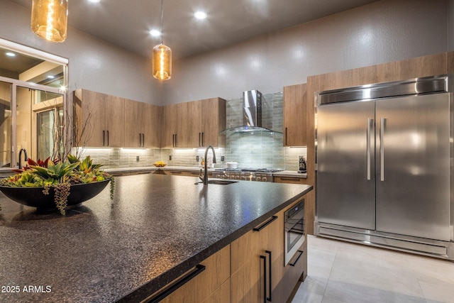 kitchen with pendant lighting, a towering ceiling, built in appliances, and wall chimney range hood