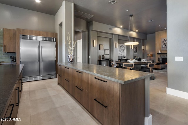 kitchen featuring a kitchen island, hanging light fixtures, tasteful backsplash, and stainless steel built in refrigerator