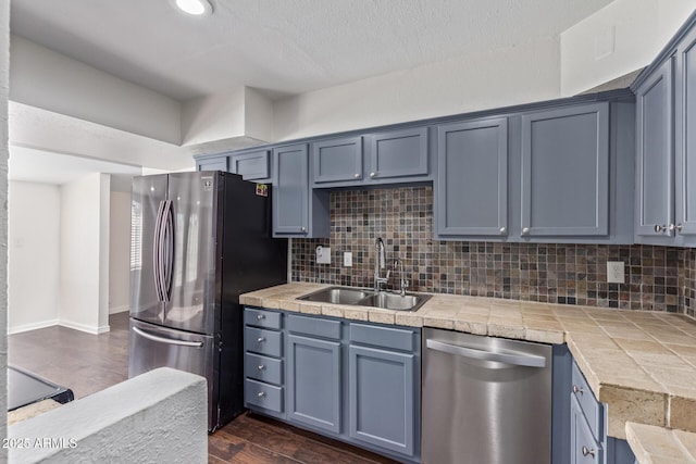 kitchen featuring dark wood finished floors, stainless steel appliances, tile counters, tasteful backsplash, and a sink