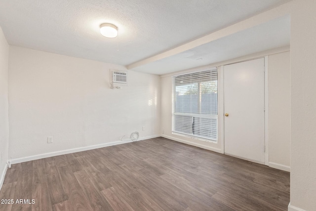 empty room featuring dark wood-style floors, an AC wall unit, a textured ceiling, and baseboards