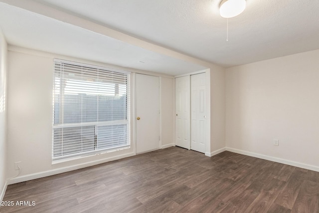 unfurnished bedroom with a textured ceiling, a closet, baseboards, and dark wood-type flooring