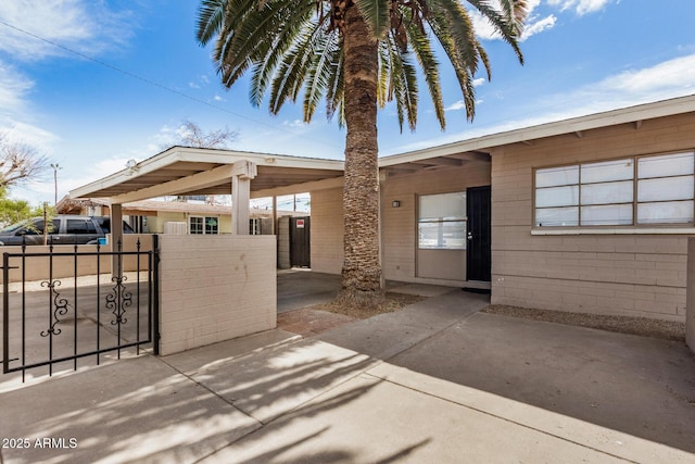 exterior space with concrete block siding, a carport, concrete driveway, and fence