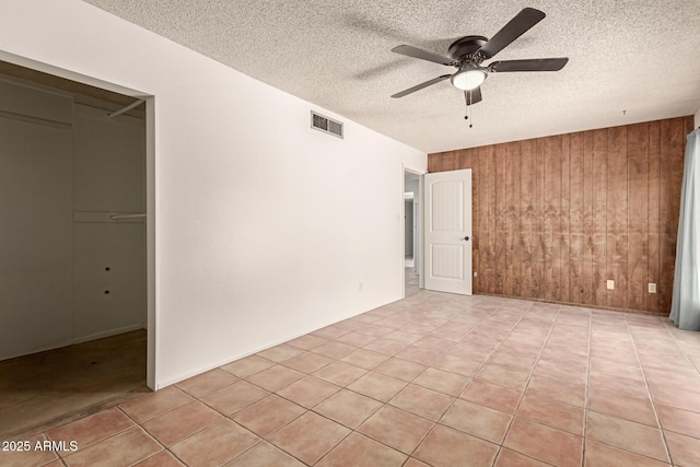 unfurnished bedroom featuring wood walls, a textured ceiling, light tile patterned floors, a closet, and ceiling fan