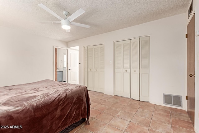 bedroom with light tile patterned floors, a textured ceiling, ceiling fan, and two closets