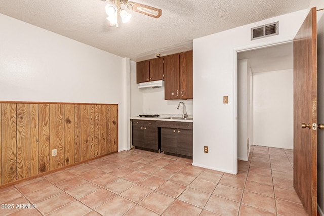 kitchen featuring wooden walls, sink, light tile patterned floors, ceiling fan, and a textured ceiling