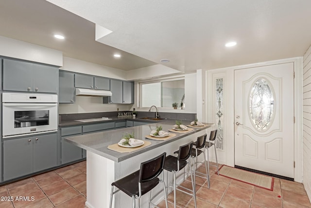 kitchen with sink, gray cabinetry, kitchen peninsula, black cooktop, and oven