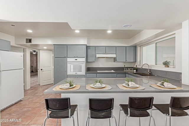 kitchen with sink, light tile patterned floors, gray cabinets, kitchen peninsula, and white appliances