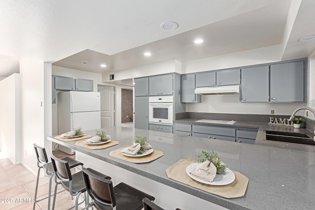 kitchen with sink, gray cabinetry, light tile patterned floors, kitchen peninsula, and white appliances