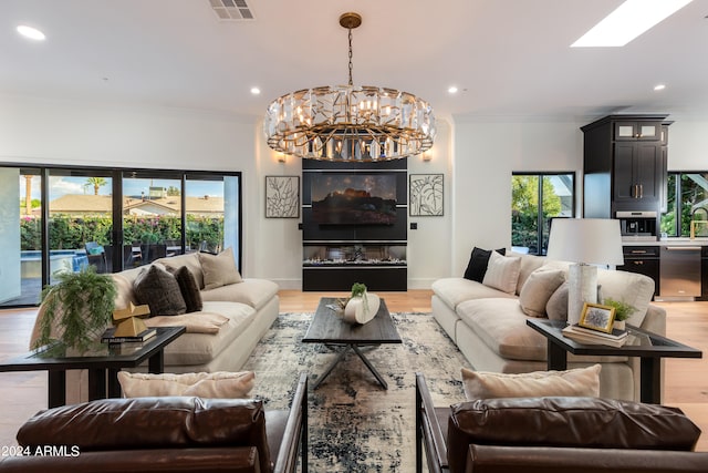 living room with crown molding, light hardwood / wood-style flooring, a chandelier, and a skylight