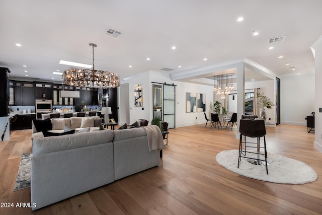 living room featuring a barn door, an inviting chandelier, light hardwood / wood-style floors, and ornamental molding